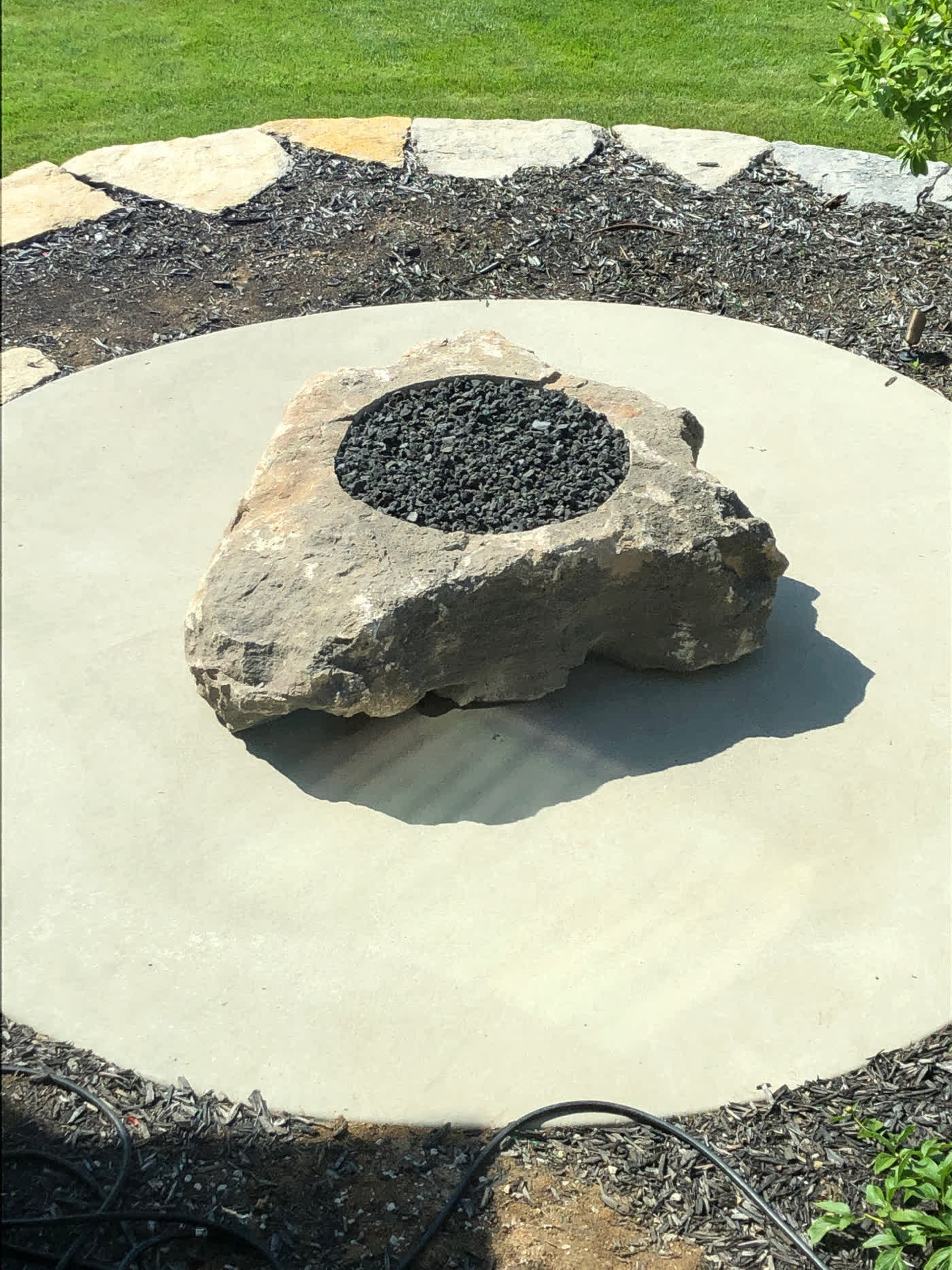 Custom gas fire rock boulder on concrete patio with natural stone border