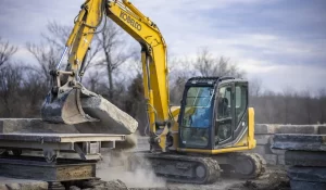 Excavator lifting heavy stone slab at construction site.