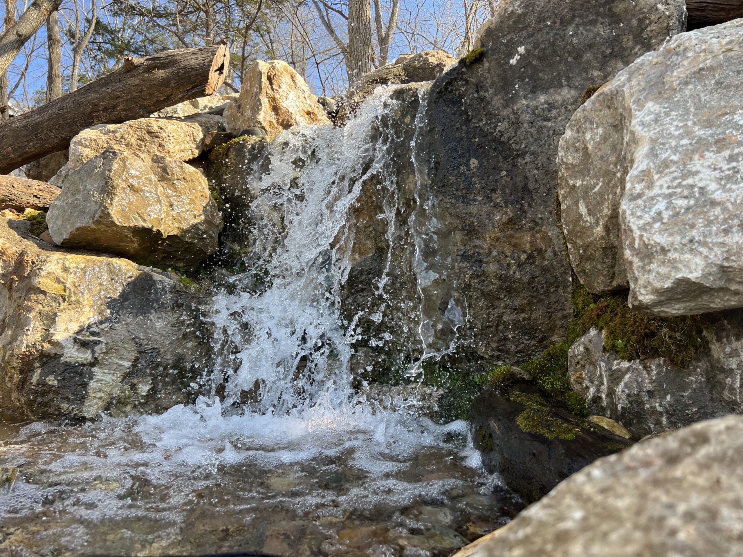 Small waterfall over rocky terrain in sunlight.